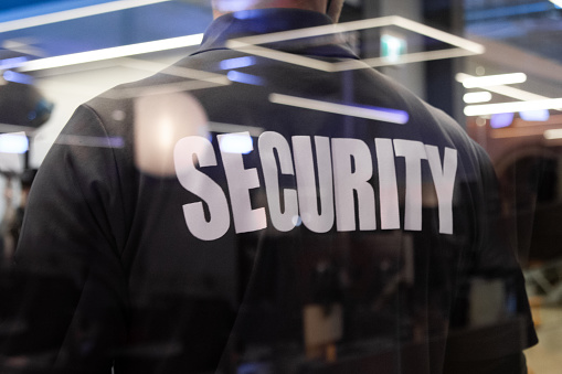 A security guard standing inside a commercial building nearby the window reflecting light.
