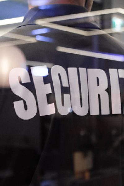 A security guard standing inside a commercial building nearby the window reflecting light.
